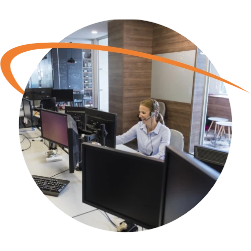 Customer support representative wearing a headset and working at a computer in a modern office with multiple monitors.